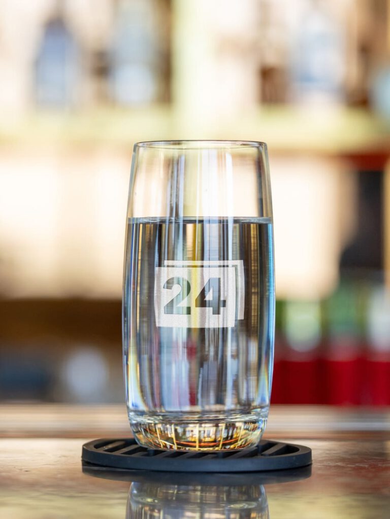 Wasserglas mit Gravur „24“ auf Theke mit hellem Hintergrund